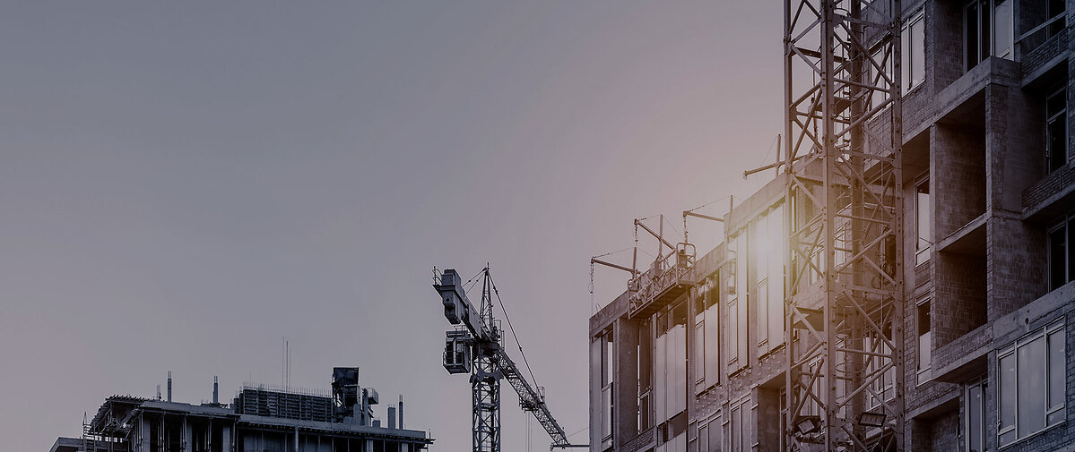 Modern apartment residential building glass facade wall construction site with many high tower cranes and heavy machinery against blue sky background. Industrial scenic urban city development project